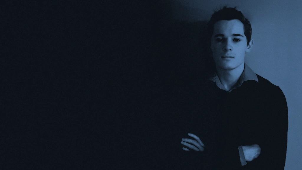 Photo de Dorian Swales, en chemise et pull chic, regardant droit devant